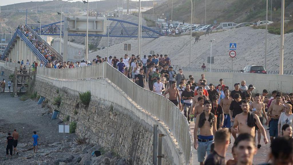 Un lungo corteo di persone cammina lungo la passeggiata sul confine di Ceuta